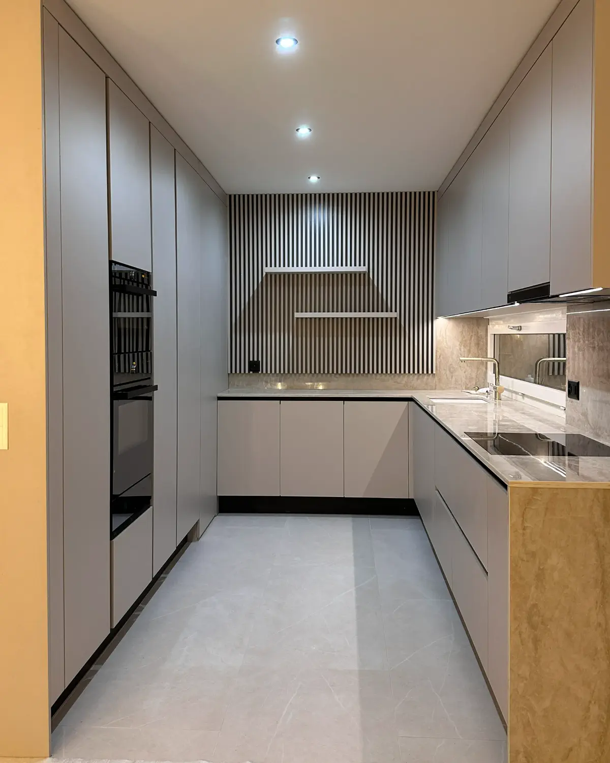 Moderne U-förmige Einbauküche mit grifflosem Design, hellen Fronten, integrierten Geräten und vertikaler Holzrückwand