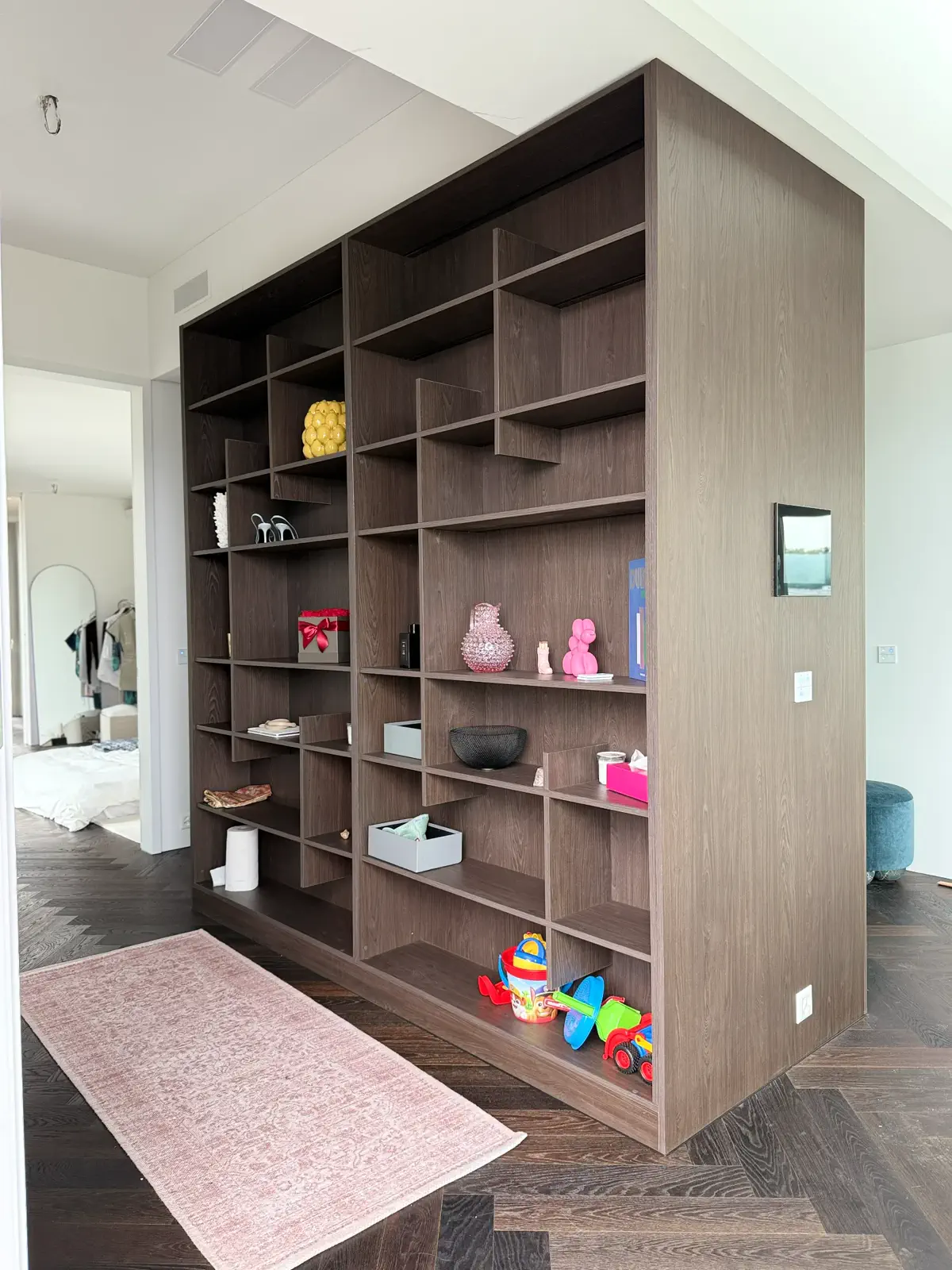 Modernes Raumteiler-Regal aus dunklem Holz mit offenen Fächern und dekorativen Elementen im Wohnbereich