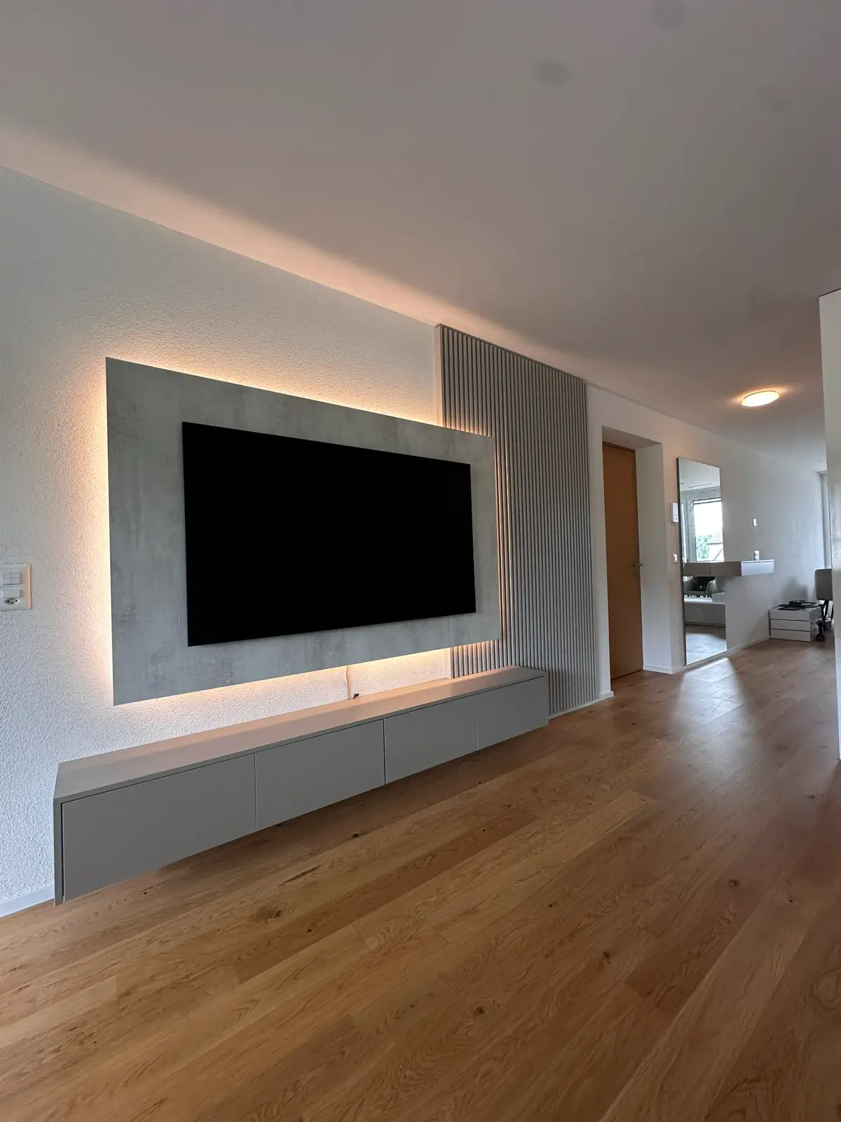 Moderne TV Kommode mit schwebendem Lowboard, indirekter LED-Beleuchtung und TV-Wand mit Lamellen im Wohnbereich